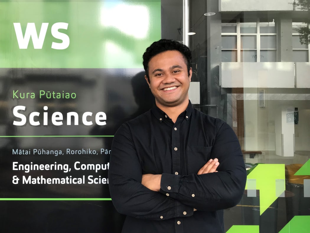 Dr Taniela Lolohea stands in front of the Science building on the AUT campus. He is smiling and has his arms folded.
