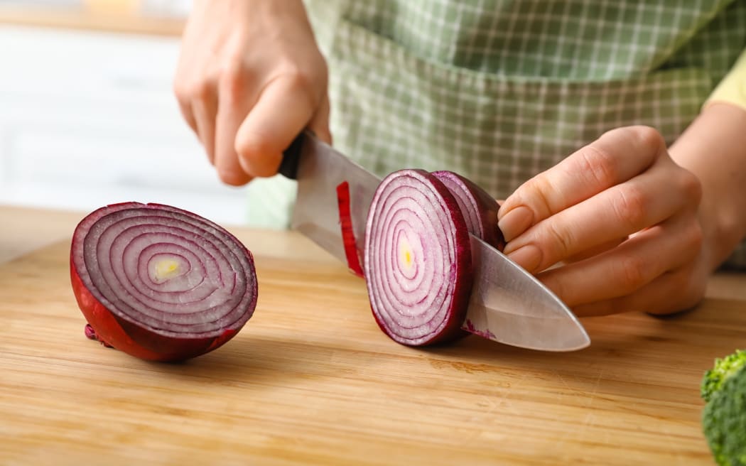 Woman cutting onion in kitchen, closeup
