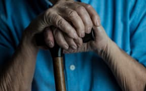 Close-up view of senior man hands leaning on a cane while sitting