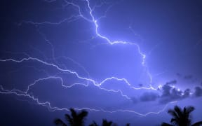 Lightning forking across the sky over trees.