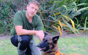 Fredrik kneels on the grass with Hawke, the dog, next to him, wearing an orange jacket.