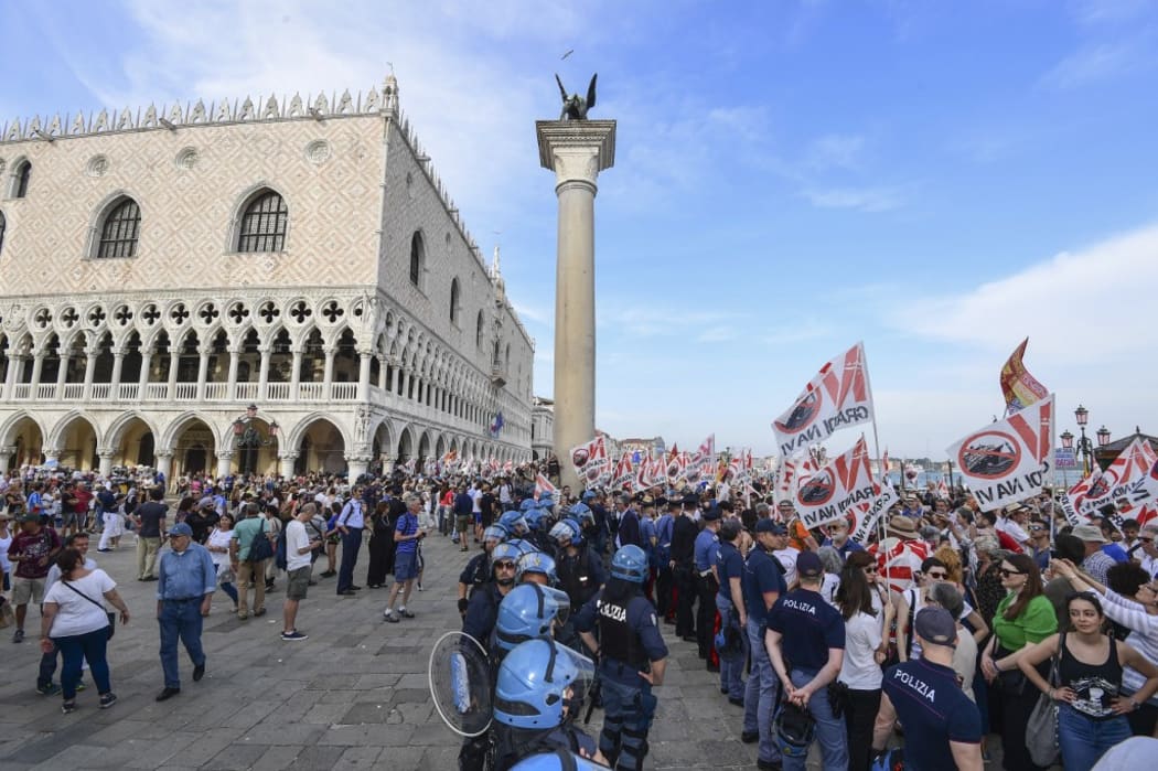 Police officers face people holding flags as they arrive close to San Marco square during a demonstration called by the No Great Ships movement against big cruise ships sailing into the Venice.
