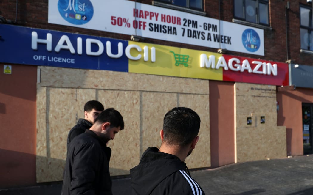 People walk past an off licence shop, boarded up and closed, ahead of an anti-immigration protest called by far-right activists, near the United Immigration Services offices at The Beacon in Newcastle-upon-Tyne, north-east England on August 7, 2024. Thousands of riot police stood ready Wednesday as Britain remained on alert for disturbances during far-right protests across the country. Nightly riots, during which mosques and migrant targets have been attacked, erupted after three children were murdered in Southport on July 29. (Photo by SCOTT HEPPELL / AFP)