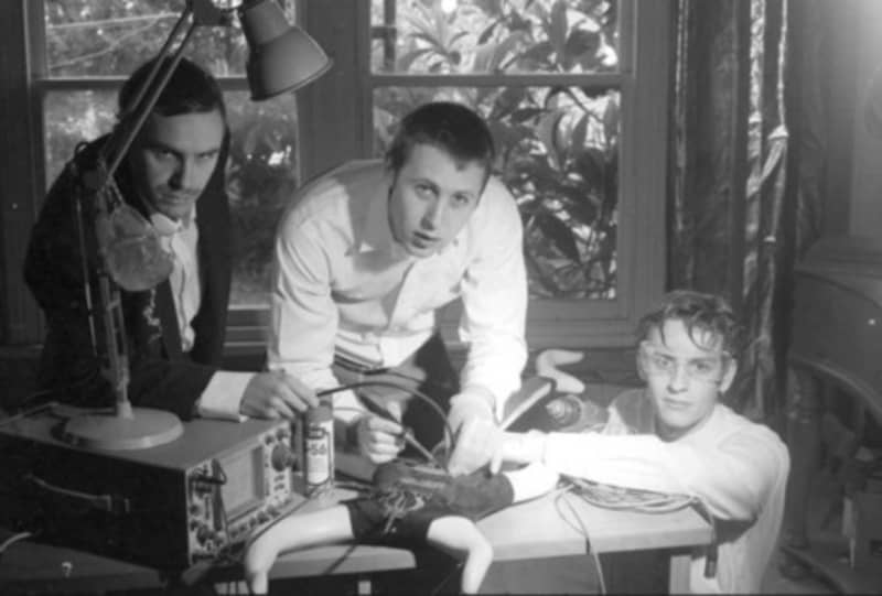 Bressa Creeting Cake are three young men huddled around a desk on which sits a strange-looking machine.