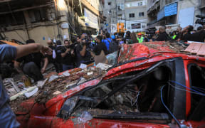 Bystanders and reporters check the destruction in a street under a residential building whose top two floors were hit by an Israeli strike in the Ghobeiri area of Beirut's southern suburbs on September 24, 2024. A Lebanese security source said on September 24 that an Israeli strike hit Hezbollah's south Beirut stronghold, as the Israel army confirmed it carried out the strike in the Lebanese capital without giving further details. (Photo by AFP)