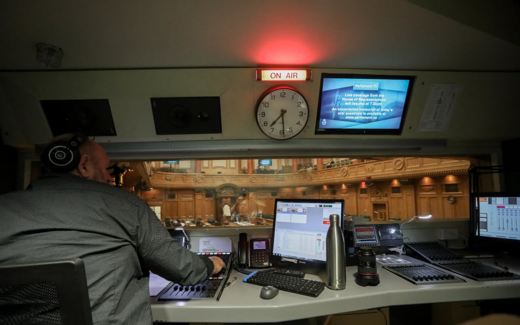 RNZ operator Colin Pearce leans into Parliament's evening sitting. In the audio booth he controls the debate audio for radio, TV and the chamber.