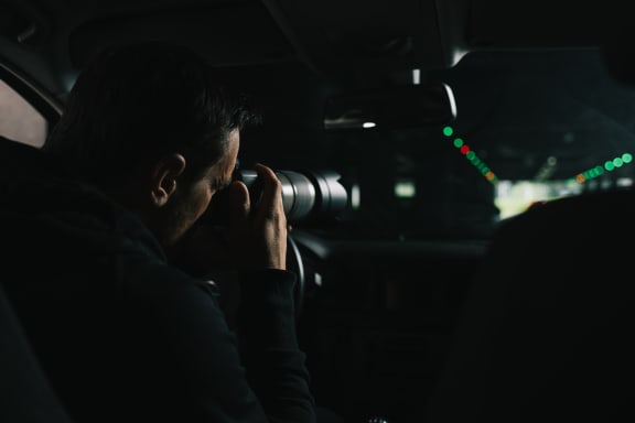 A generic photo of a man in his car doing surveillance with a camera.