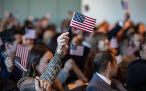 People wave US flags to celebrate becoming US citizens after taking the oath of allegiance during a naturalization ceremony in the jury assembly room at the John Joseph Moakley United States Courthouse in Boston, Massachusetts on January 8, 2025. In total 102 immigrants from 40 countries became US citizens during the ceremony. (Photo by Joseph Prezioso / AFP)