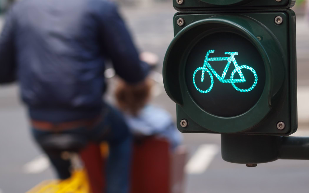 A cyclist passes a green cycling traffic light in a city.