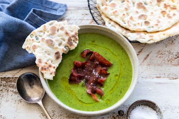 A bowl of bright green pea, spinach and tarragon soup garnished with crisp bacon and seedy yoghurt flatbreads.