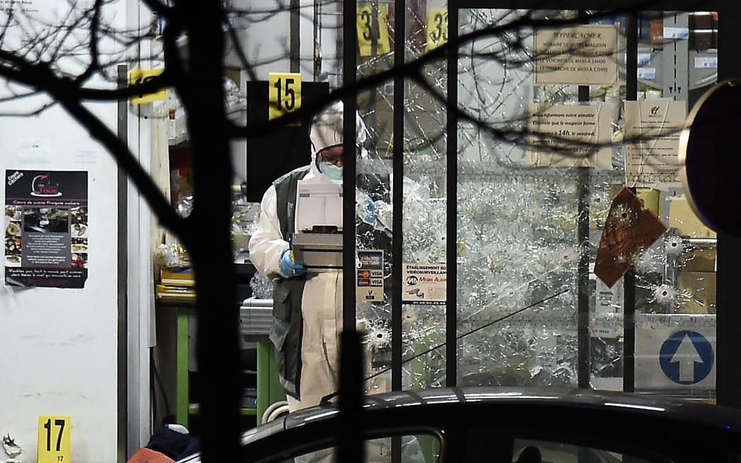 A forensic police officer works next to the bullet-riddled windows of the Hyper Casher kosher supermarket.
