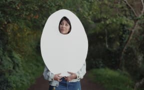Director Shamin Yazdani holds up a cardboard cutout of an egg shape.