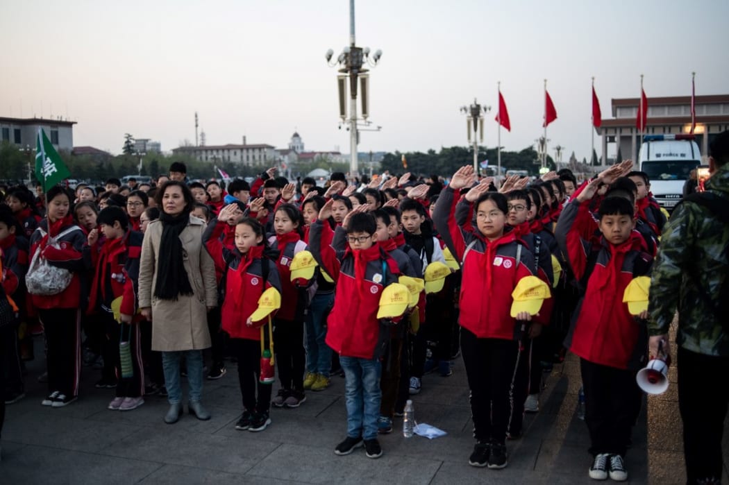 In this picture taken on April 1, 2019, school students sing the national anthem at Tiananmen square in Beijing. - Thirty years after the crackdown on Tiananmen protesters, the tanks that lined Beijing's central avenue have been replaced by countless surveillance cameras