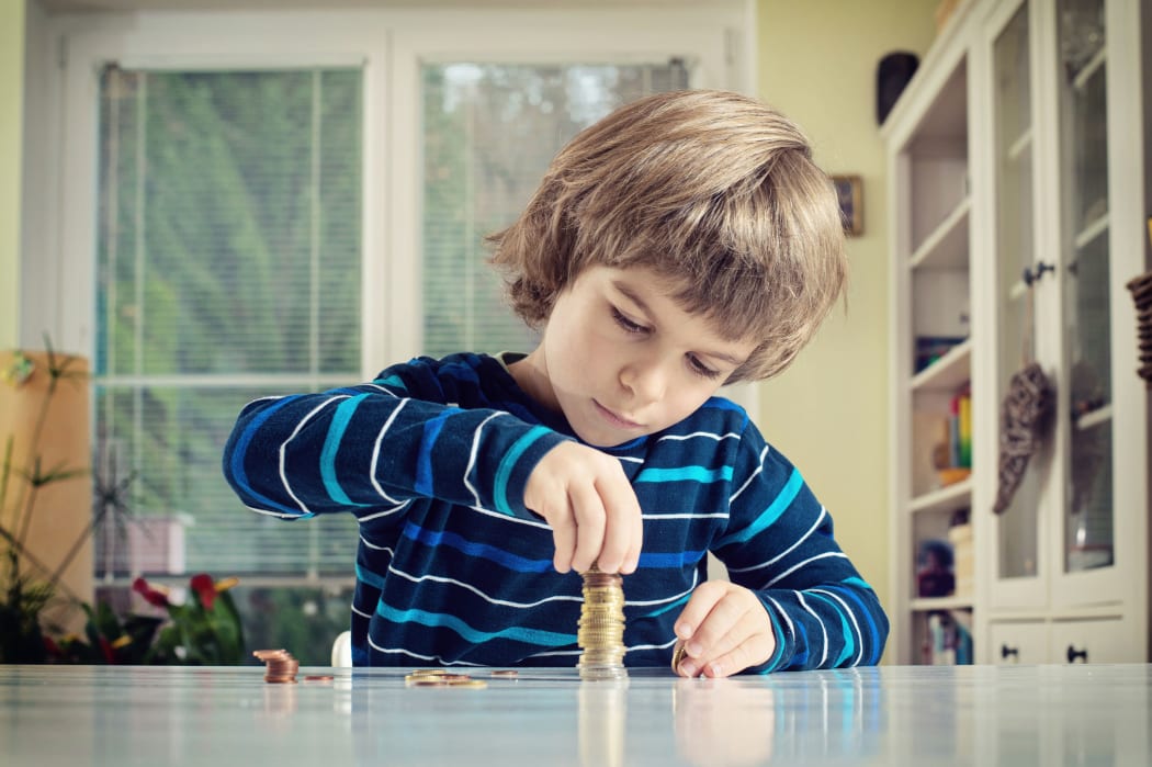 A photo of a little boy making stack of coins, counting money at table. Learning financial responsibility and planning savings concept.