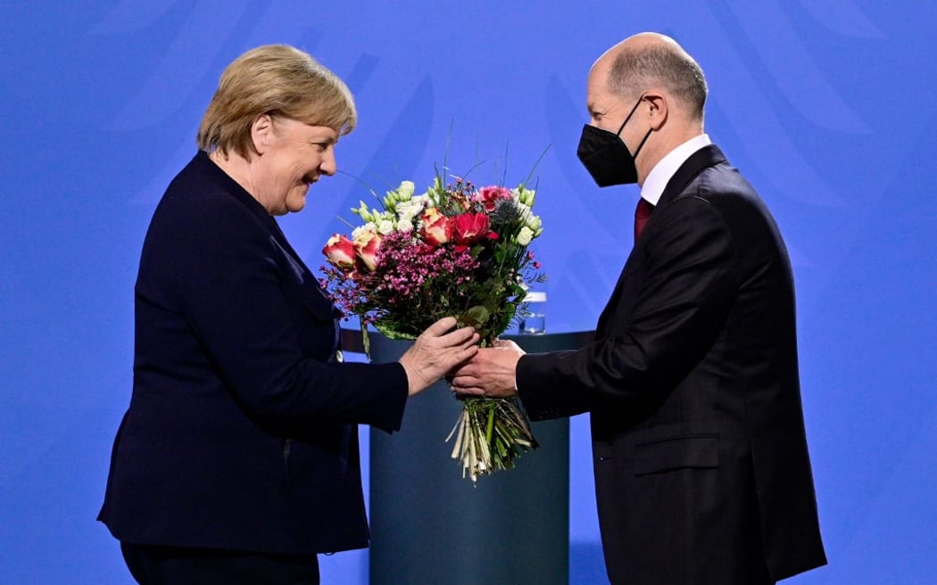 German Chancellor Olaf Scholz gives a bouquet of flowers to his predecessor Angela Merkel after she handed him over the office at the Chancellery in Berlin