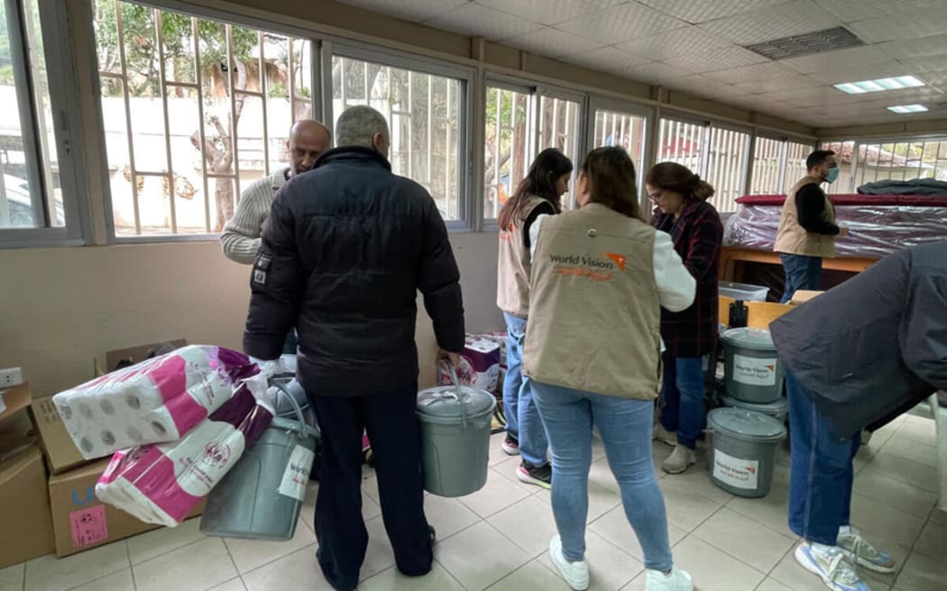 People stand holding supplies, including buckets and toilet paper in an aid shelter in Lebanon.