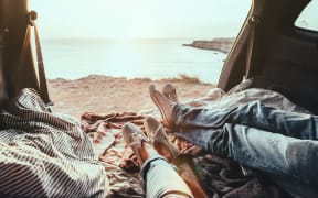 Man and woman relaxing inside trunk and watching at the sea. Fall car trip in sunset. Freedom travel concept. weekend.