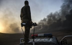 A member of the Iraqi government forces takes a position on top of a vehicle as smoke rises on the outskirts of the Qayyarah area, some 60km south of Mosul