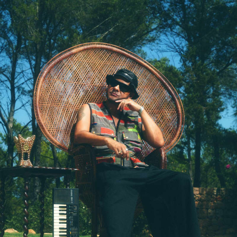 A relaxed man sits in a wicker chair outside.