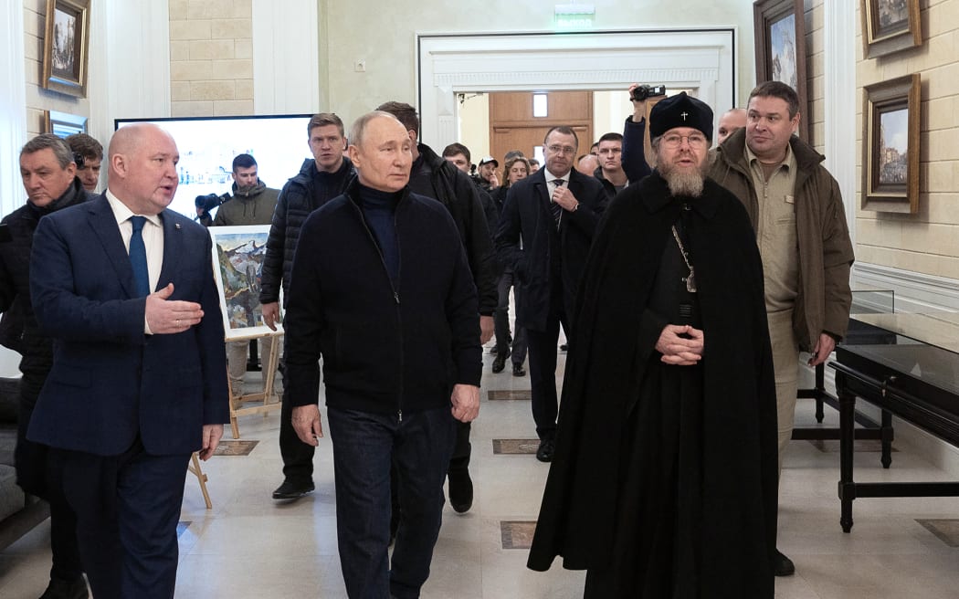 This handout photograph taken and released by the Russian presidential press office in Sevastopol on March 18, 2023, shows Russian President Vladimir Putin (C), flanked by Metropolitan Tikhon Shevkunov (R), chairman of the Patriarchal Council for Culture, listening to Sevastopol Governor Mikhail Razvozhayev (L), as he visits the Chersonesos Taurica historical and archeological park on the 9th anniversary of the referendum on the state status of Crimea and Sevastopol and its reunification with Russia.