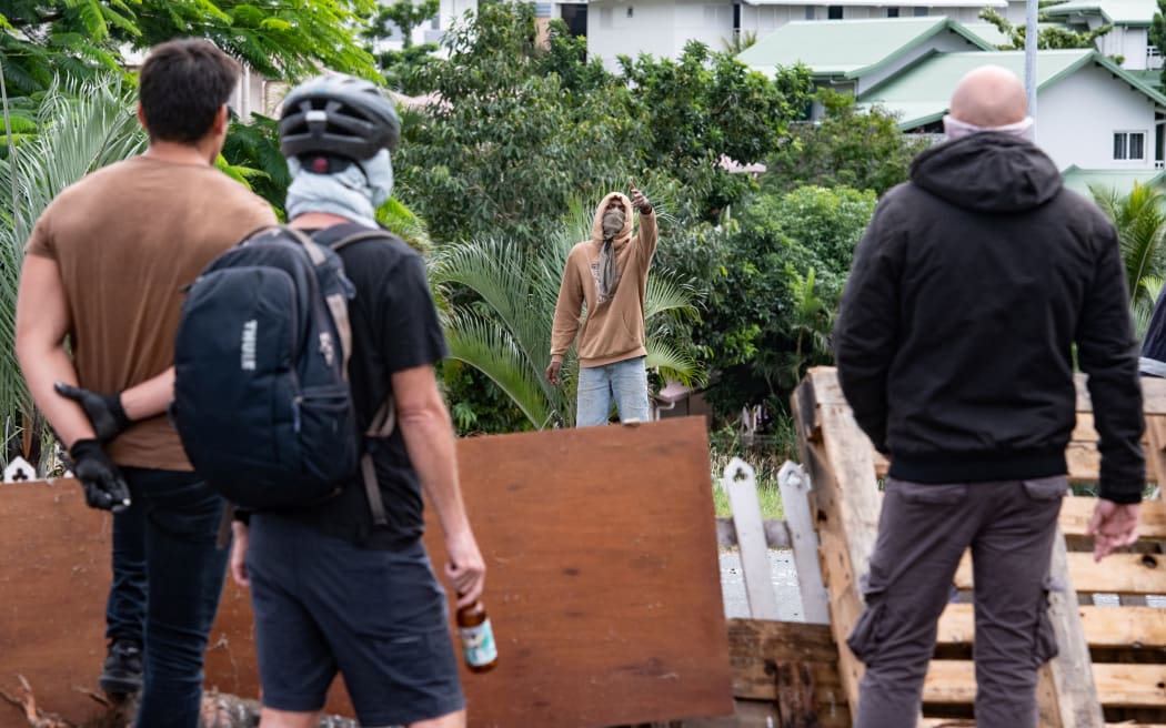 Masked residents watch an activist at the entrance to Tuband, in the Motor Pool district of Noumea on May 15, 2024, amid protests linked to a debate on a constitutional bill aimed at enlarging the electorate for upcoming elections of the overseas French territory of New Caledonia. One person was killed, hundreds more were injured, shops were looted and public buildings torched during a second night of rioting in New Caledonia, authorities said Wednesday, as anger over constitutional reforms from Paris boiled over. (Photo by Delphine Mayeur / AFP)