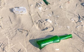 boot prints on the sand beach and man-thrown green glass bottle. concept of environmental pollution.