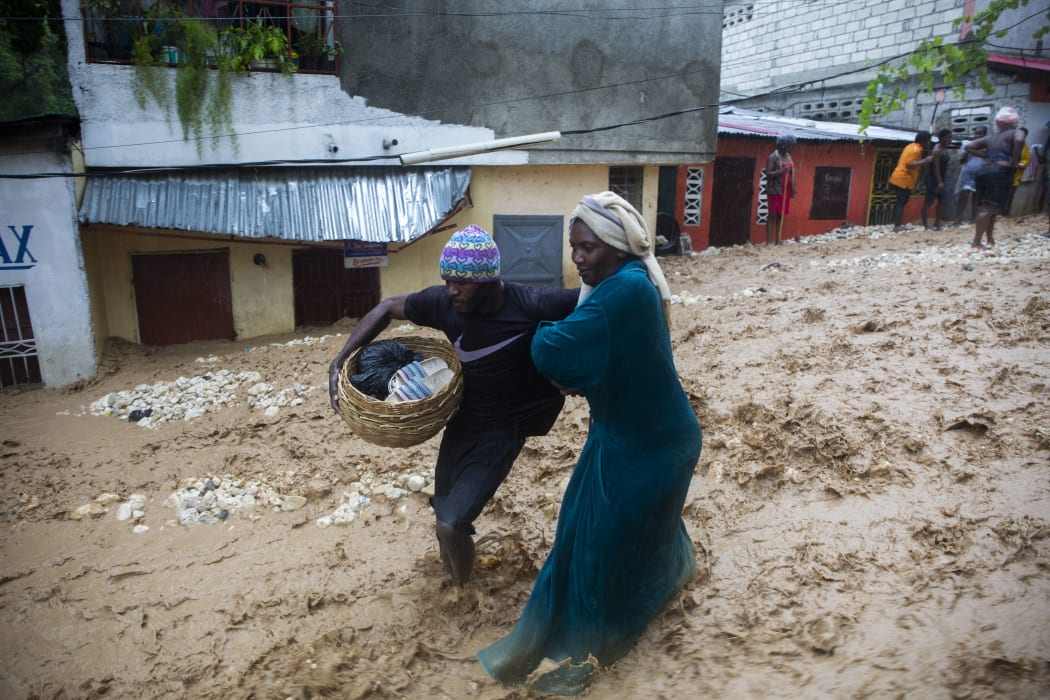 People walking through a flooded street in Pétion ville, Haiti, on 23 August during the passage of  Tropical Storm Laura. Heavy rains hammered Haiti, killing at least five people.