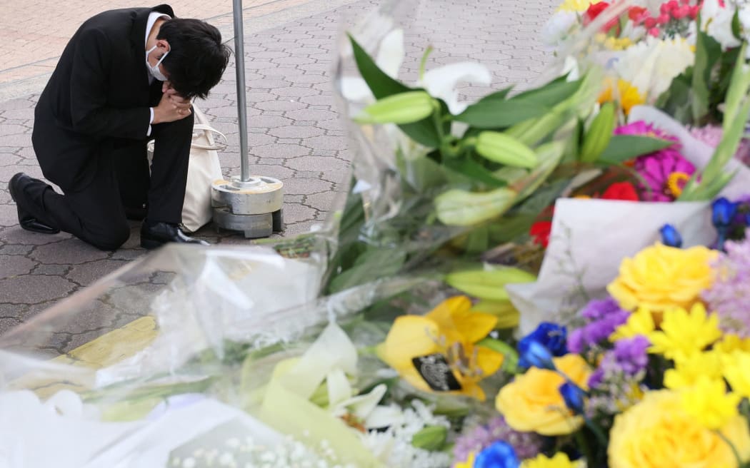 People offer flowers and prayers near a site where former Prime Minister Shinzo Abe was shot to death near Yamato Saidaiji Station in Nara Prefecture on July 9, 2022.Former Prime Minister Shinzo Abe was the victim of a fatal gun attack while taking part in a campaign event for the House of Councillors election in Nara City on the same day. He was 67. After being shot at around 11:30 a.m., he was confirmed dead at 5:03 p.m. at Nara Medical University Hospital in Kashihara, Nara Prefecture, where he was transported by ambulance and a medical helicopter immediately after the attack. Yamagami, 41, of Nara City, was arrested at the scene on suspicion of attempted murder at 11:32 a.m. Yamagami is believed to have shot Abe at close range and a gun has been recovered, according to a police officer.  ( The Yomiuri Shimbun ) (Photo by Naoki Maeda / Yomiuri / The Yomiuri Shimbun via AFP)