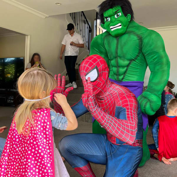 Kids party entertainment company A Couple of Characters founder Jeandre Zwart dressed as Spider-Man and another person dressed as The Hulk interact with a little girl at a party.