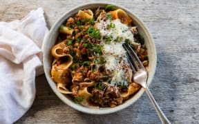 A round bowl of pasta with bolognese sauce, topped with finely grated cheese and thinly sliced spring onions.