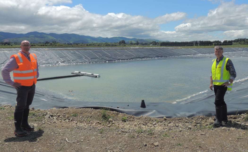 Carterton District Council infrastructure, services, and regulatory manager Dave Gittings and chief executive Geoff Hamilton with a wastewater pond behind them. The pond has rainwater in it after a heavy downpour.