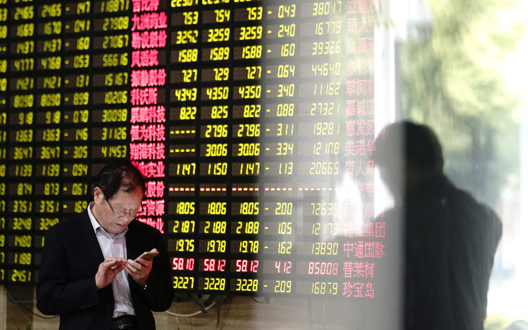 A man looks at his smartphone near a display showing stock prices at a brokerage house in Shanghai 6 May 2019.