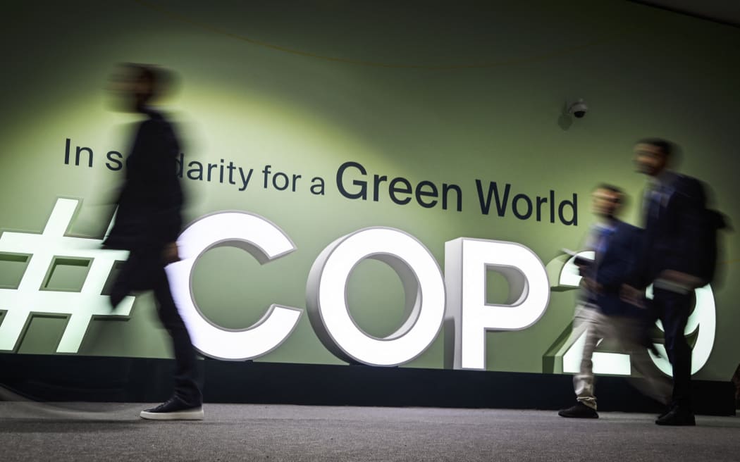 People walk past the logotype at the venue for the 2024 United Nations Climate Change Conference (COP29) in Baku on November 11, 2024.