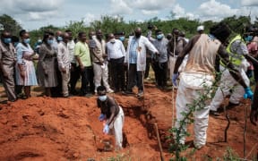 Workers dig the ground to exume bodies as Kenya's Interior Minister Kithure Kindiki  visits the mass-grave site in Shakahola, outside the coastal town of Malindi, on April 25, 2023. Kenyan investigators unearthed another 16 bodies on Tuesday in a forest where a cult was believed to be practising mass starvation, bringing the number of victims so far to 89 including children. There are fears more corpses could be found in Shakahola forest where cult leader Paul Mackenzie Nthenge had allegedly been telling his followers that starvation was the only path to God. (Photo by Yasuyoshi CHIBA / AFP)