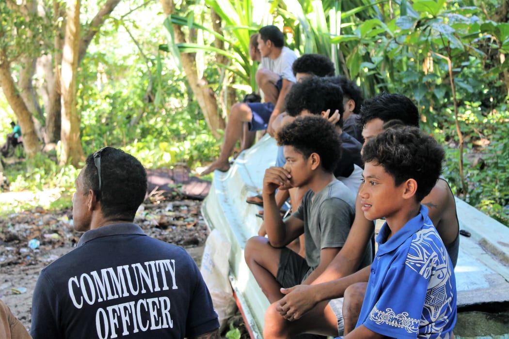 A community officer speaks with youth while watching a sports event in Rennell Bellona province.