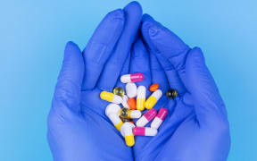 Different pills in hand in a medical glove on a blue background. Medicine. Treatment. Prevention