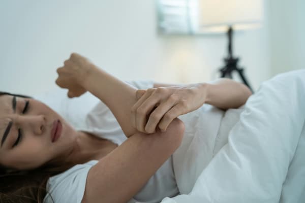 A woman lying in bed and itching her arm.