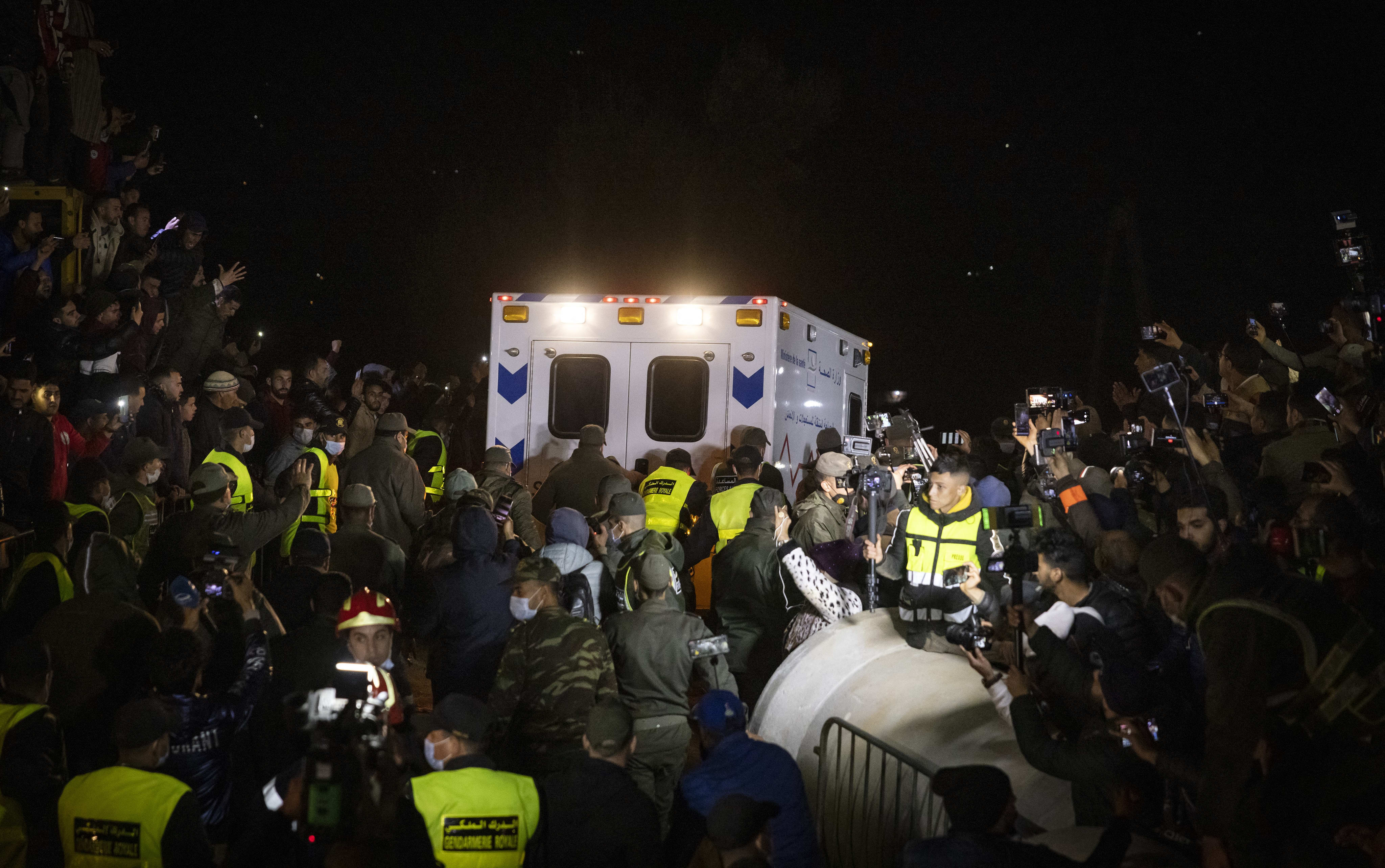 Rescuers and spectators look on as an ambulance drives away from the rescue scene.