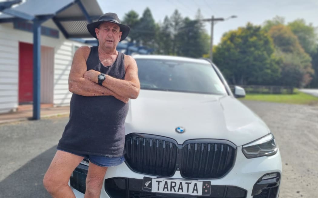 Unofficial mayor of Tarata Bryan Hocken stands infront of a car with the numberplate displaying 'Tarata'.