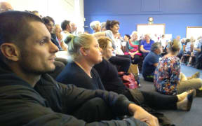 Paul Chronis and Charlotte Boocock sit on the church hall floor at a packed Island Bay meeting.