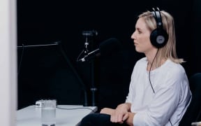 Journalist Anna Burns-Francis with headphones on sitting in front of a microphone.