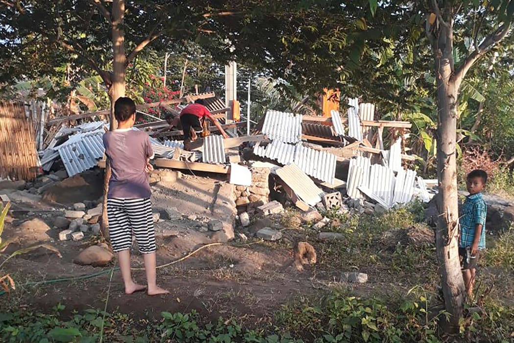 Indonesians scramble over the collapsed ruins of a house as others look on following an earthquake in Lombok.