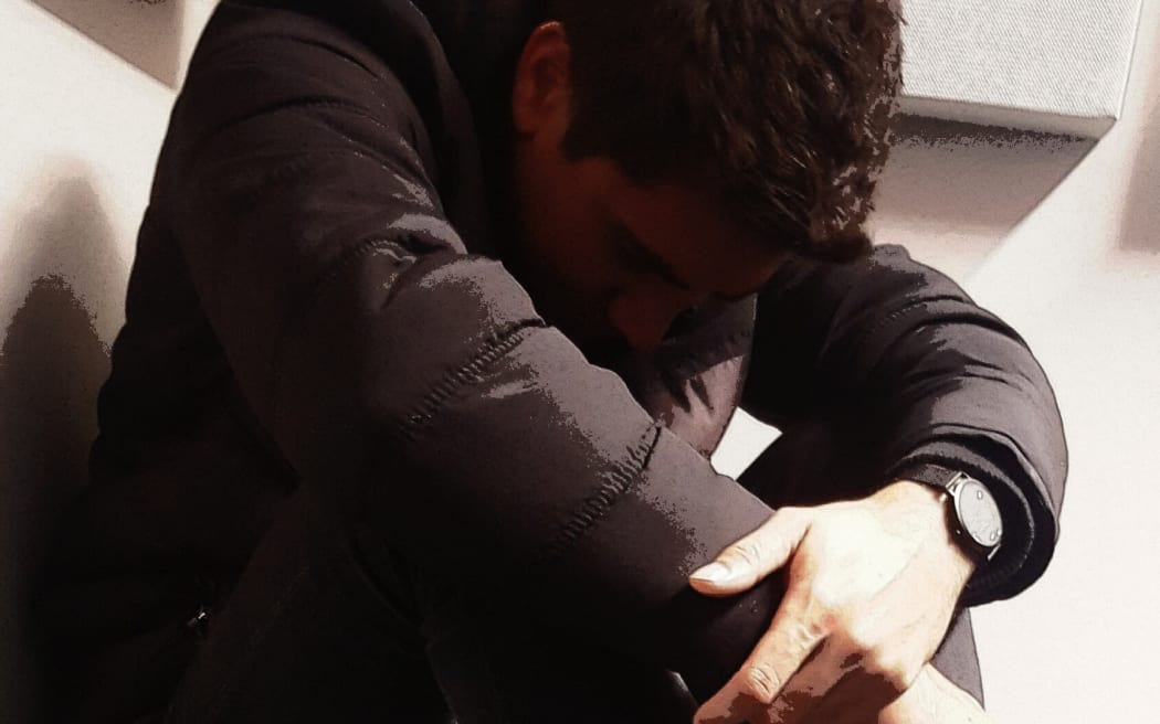 A staged photo of a young man hunched over, used to illustrate the use of seclusion rooms or mental health issues.