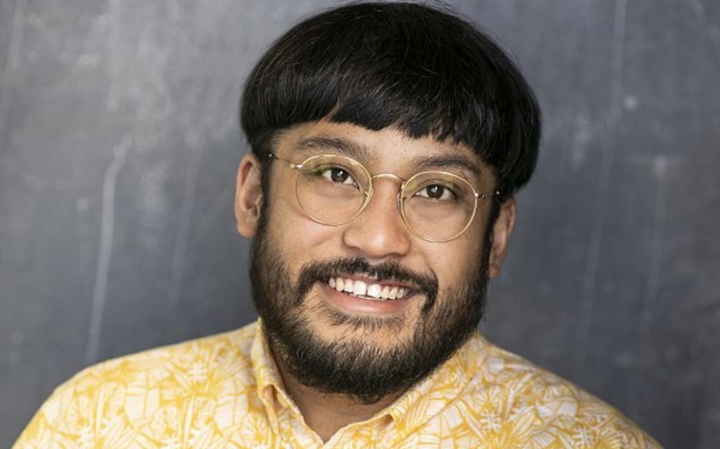 David smiles at the camera. He wears a yellow patterned shirt and gold-rimmed glasses.