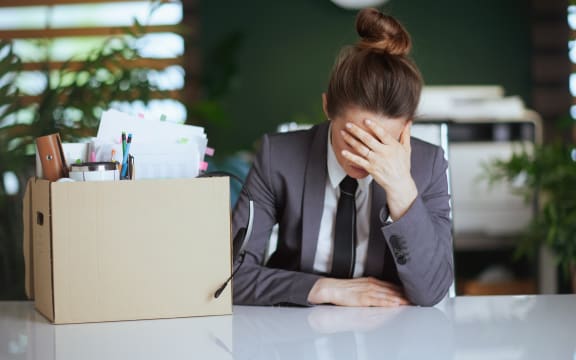 Stressed modern woman worker in modern green office in grey business suit with personal belongings in cardboard box.