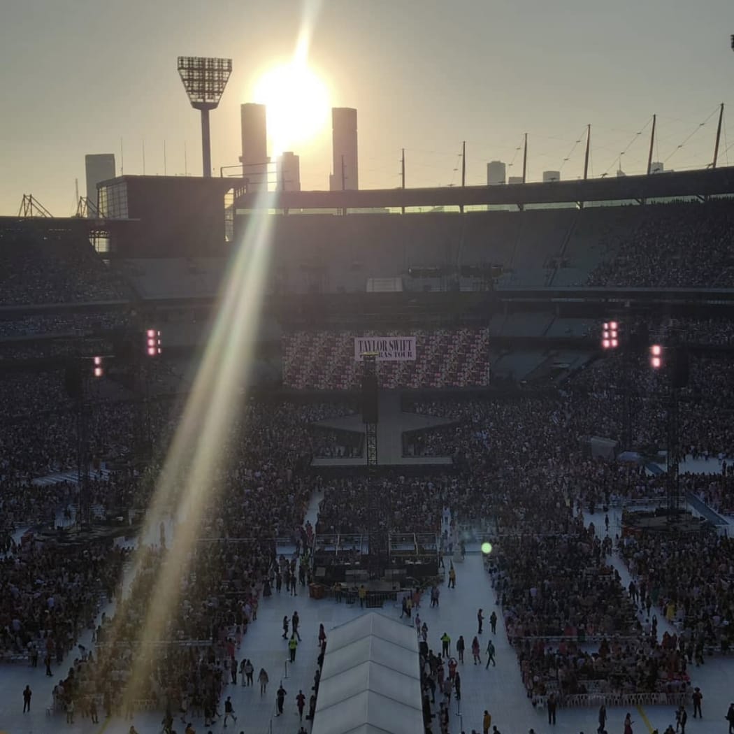 A large stadium with thousands of people. The sun goes down over the rim.