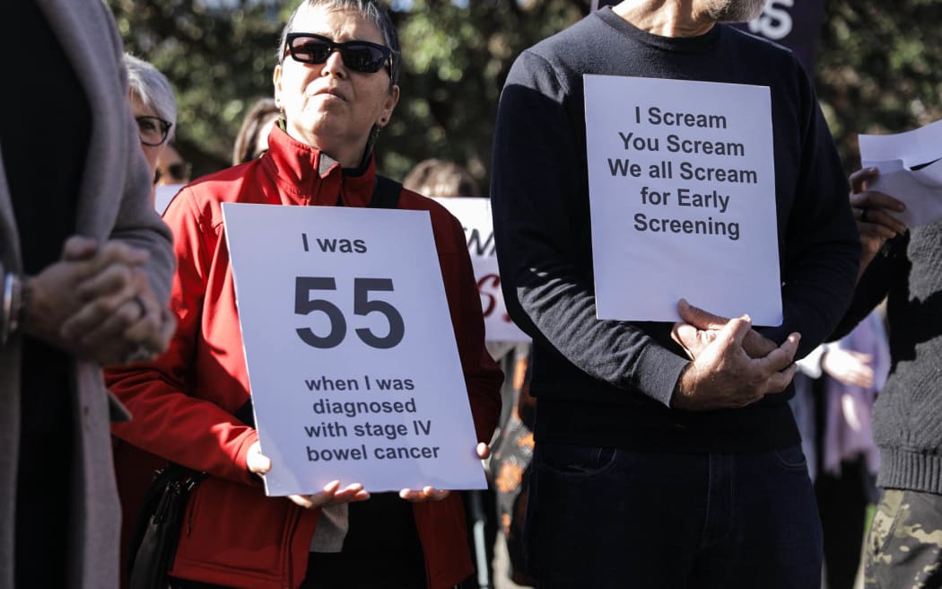 Bowel cancer protestors hold signs outside Parliament