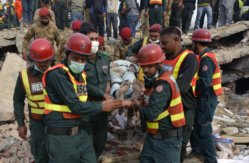 Pakistani rescuers move a man rescued from under the rubble of the collapsed factory.