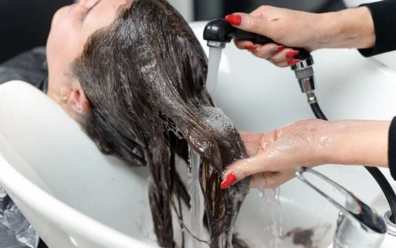 Hairdresser washing hair of a woman in a beauty salon. Water restrictions affecting businesses.