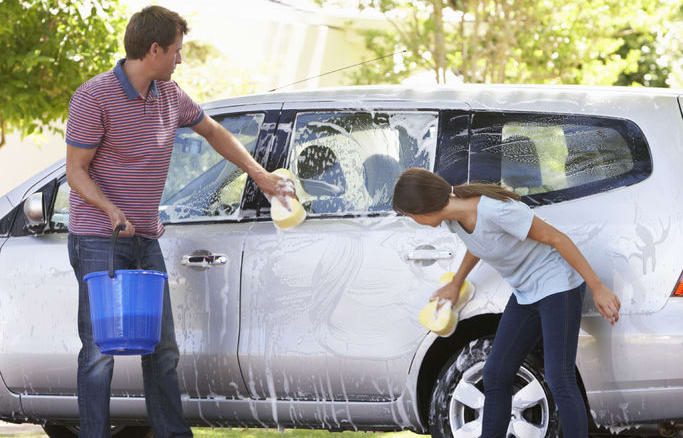 A photo of a father washing his car with histeenage daughter